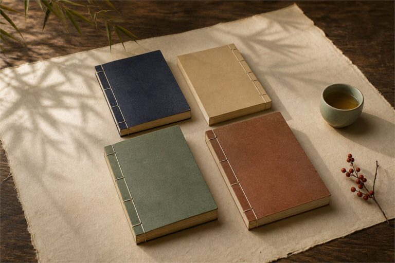 Four blank thread-bound classical books arranged on ivory cloth beside a ceramic cup