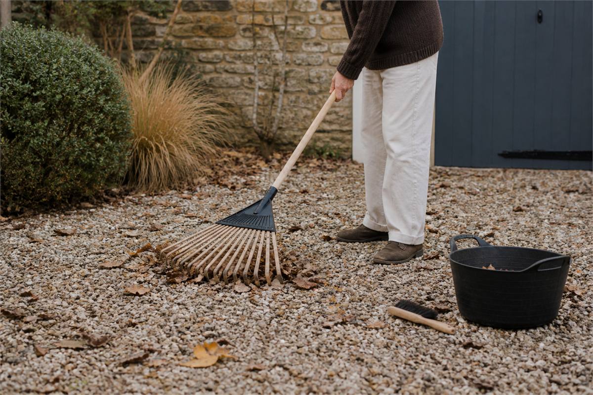 Gardener using a soft leaf rake to collect dry leaves from decorative gravel