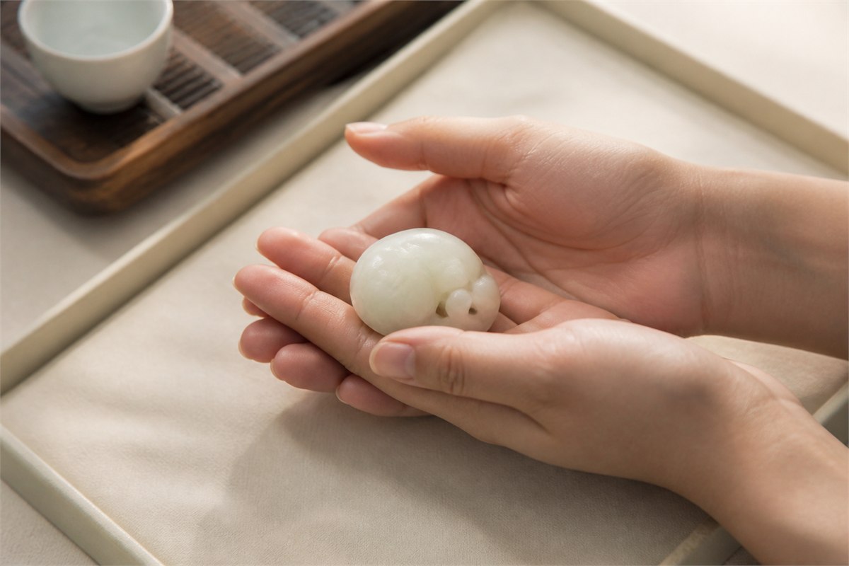 Relaxed adult hands lightly cradle a small creamy nephrite carving above a padded tray.