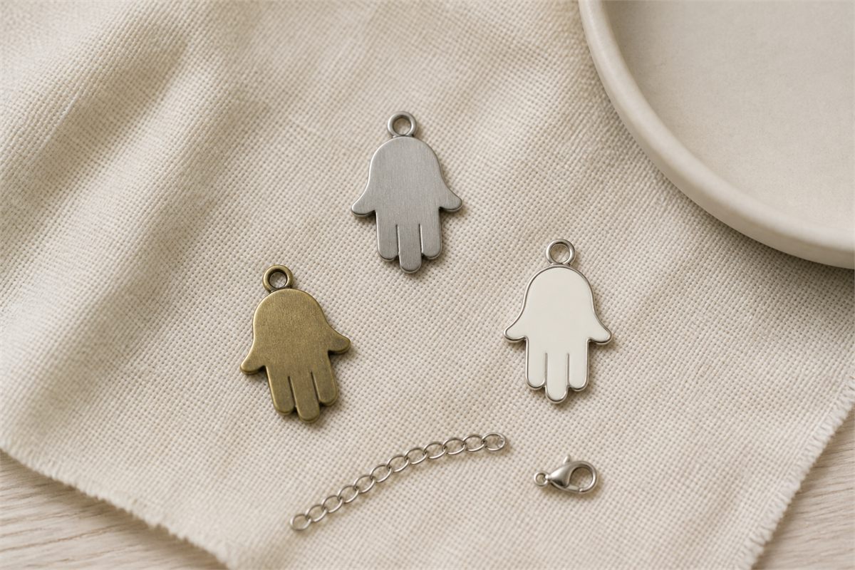 Silver-tone, brass, and cream enamel Hamsa charms with a chain sample and clasp on linen