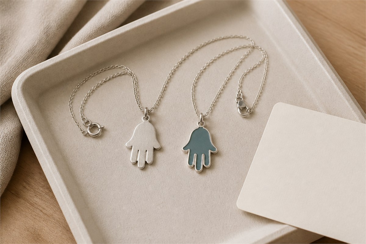 Plain silver and muted teal enamel Hamsa pendants with separate chains beside a blank card