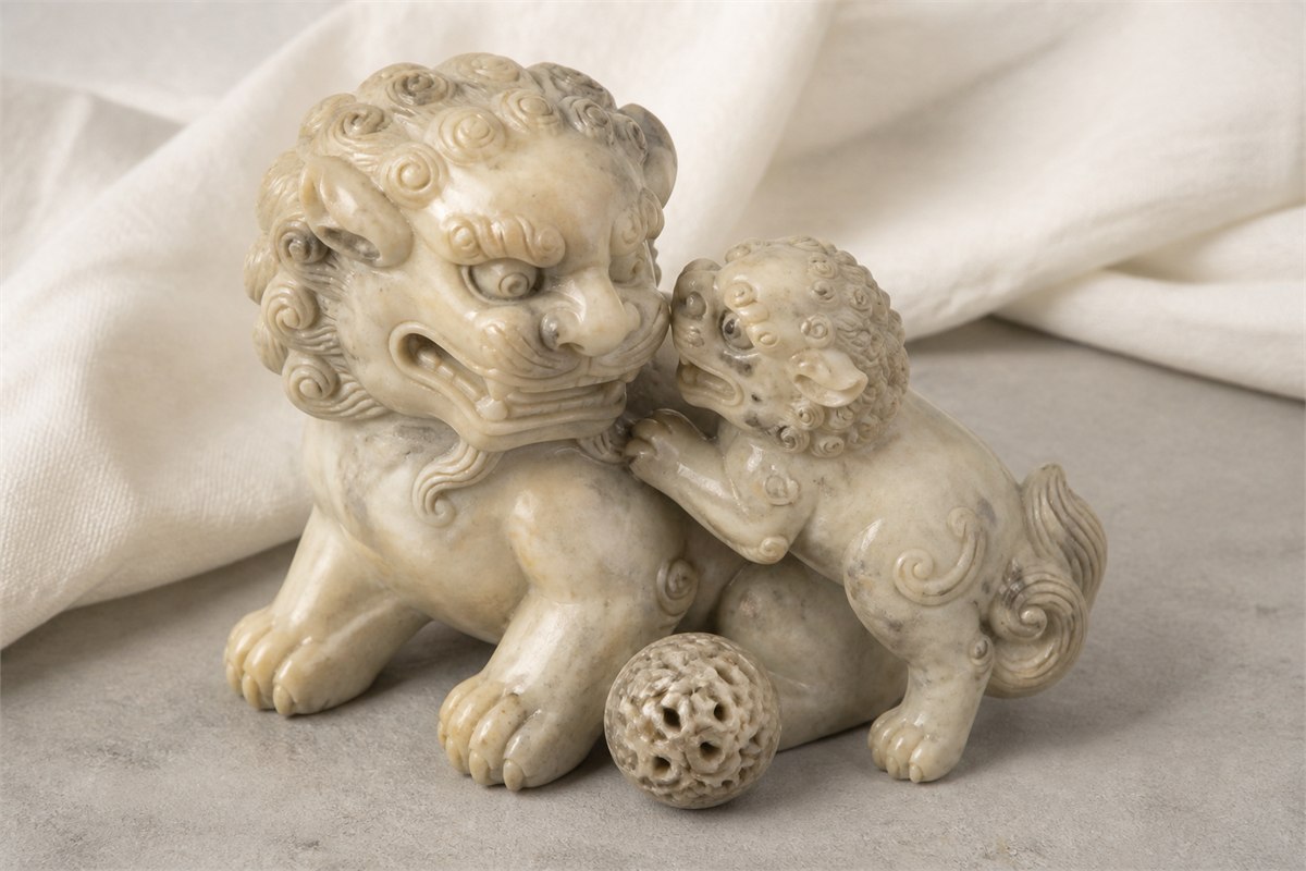 Close view of one large stone lion and one smaller cub beside a carved brocade ball
