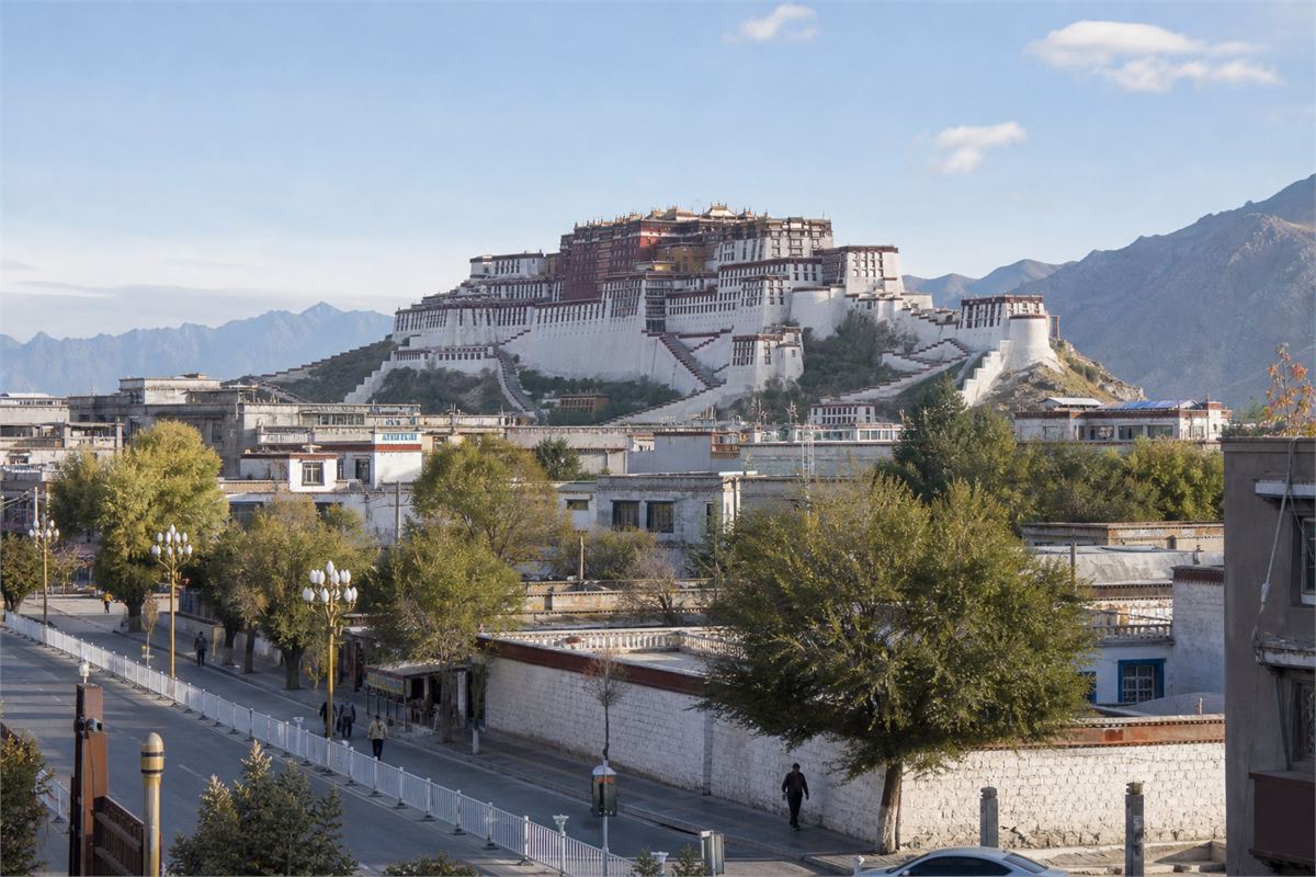 The Potala Palace above a quiet Lhasa street with homes, trees, and pedestrians