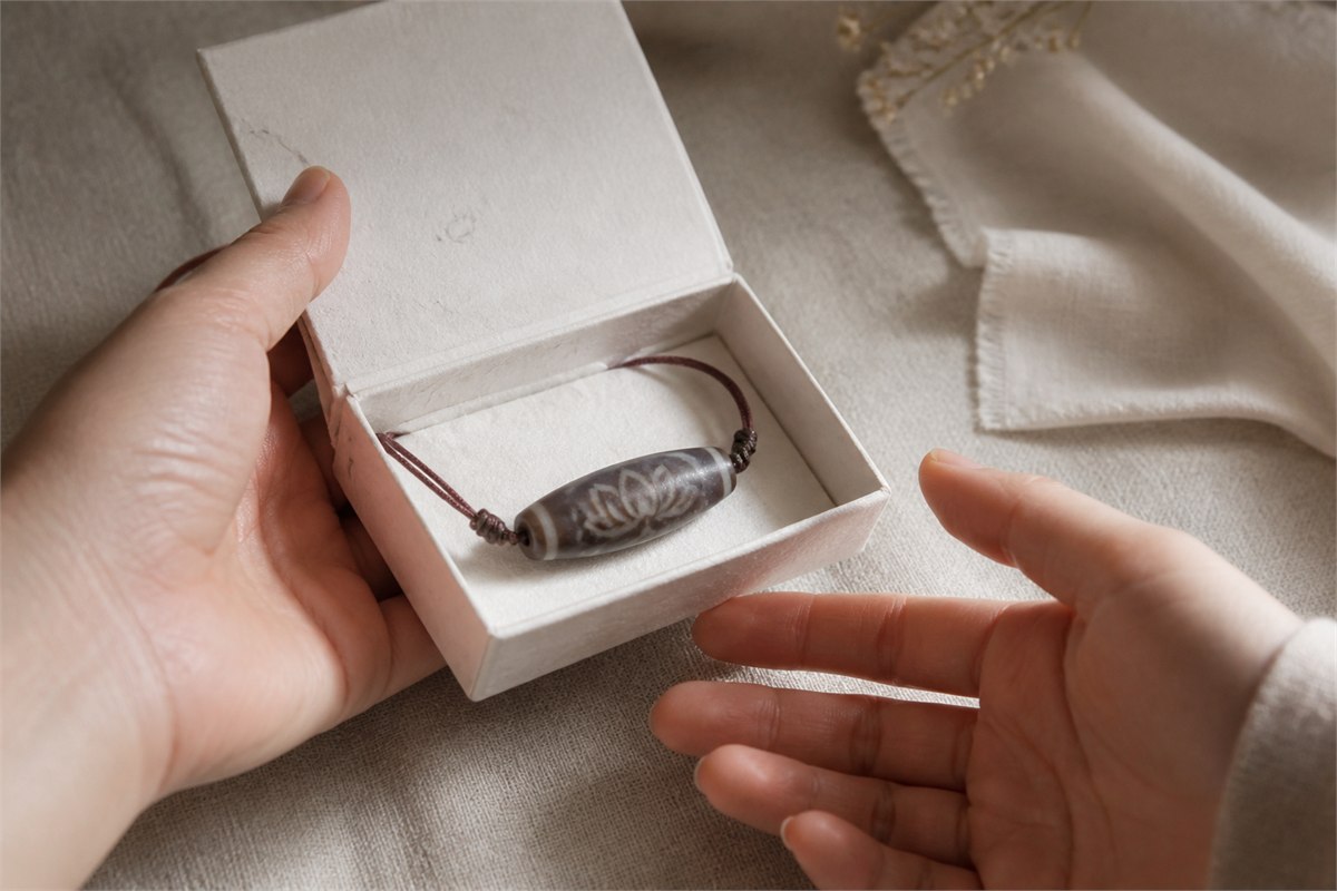 Lotus-pattern agate Dzi-style pendant in an ivory gift box held between two hands