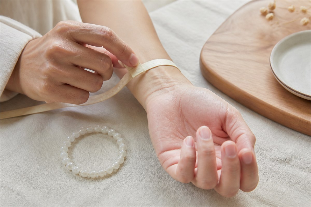 Flexible measuring tape wrapped gently around a wrist with a moonstone bracelet nearby