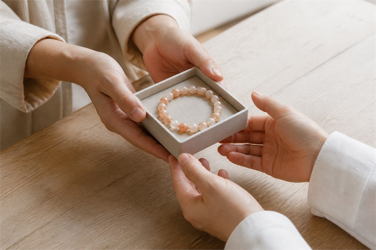 Two people exchanging a soft-lined box with a peach and white moonstone bracelet