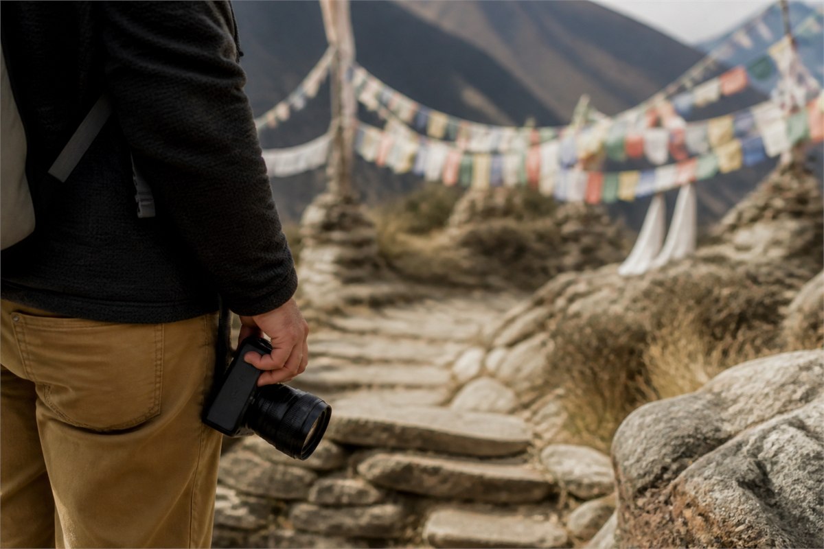 Traveler holding a lowered camera at a distance from blurred mountain prayer flags