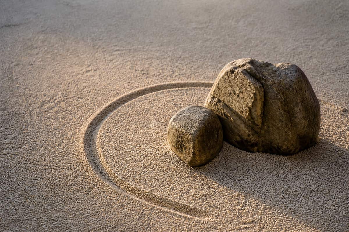 Two natural stones beside a freshly swept curved line in pale gravel