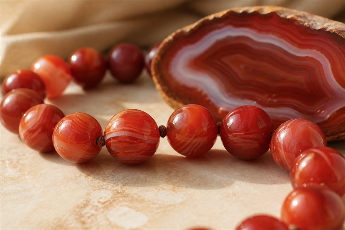 Strung red agate beads beside a polished agate slice showing curved chalcedony bands