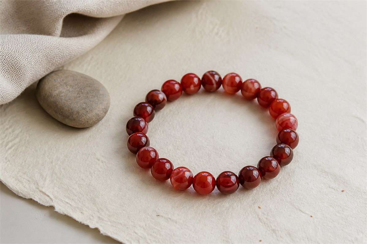 Red agate bead bracelet with varied translucent red bands on warm ivory paper