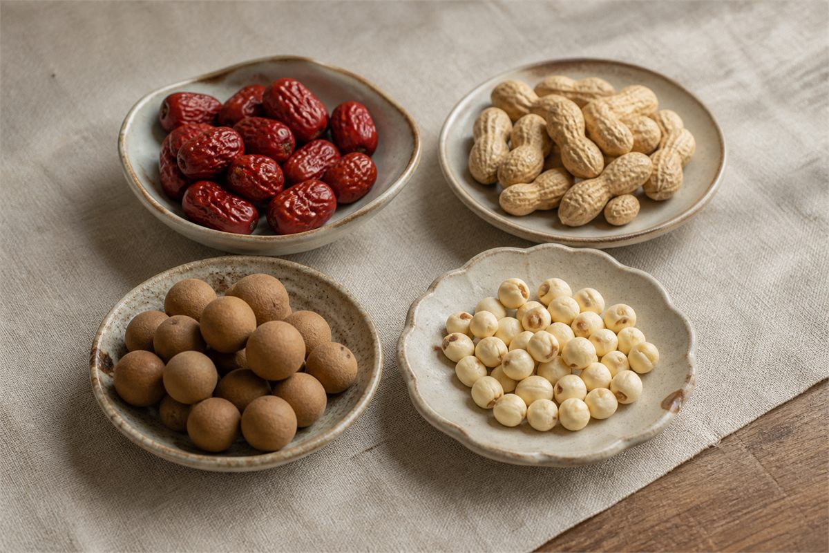 Four ceramic dishes holding red dates, peanuts, dried longans, and lotus seeds