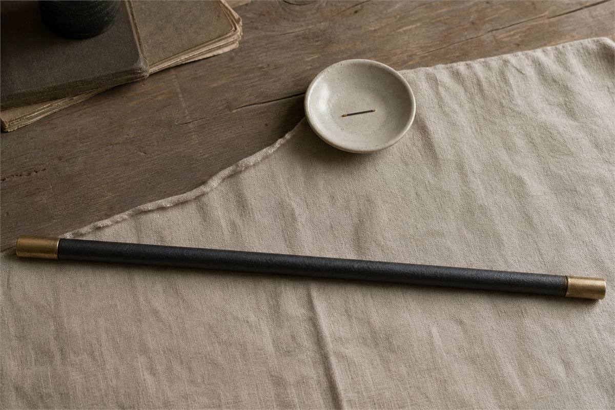A full-size dark iron staff with golden tips and a needle-sized matching form in a ceramic dish