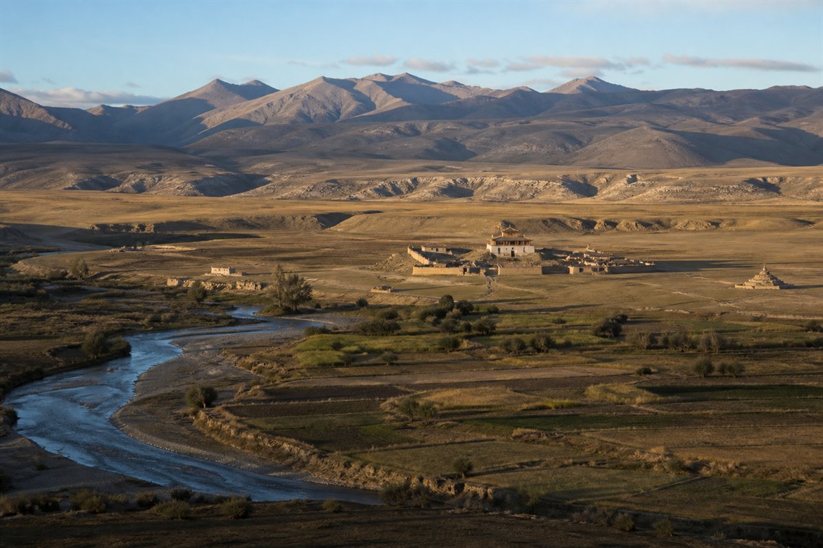 Distant monastery compound in a broad highland river valley under morning light