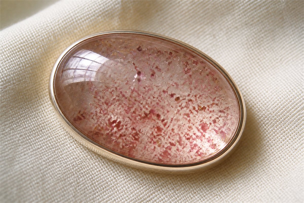 Close view of a strawberry quartz cabochon with red and pink flakes at different depths
