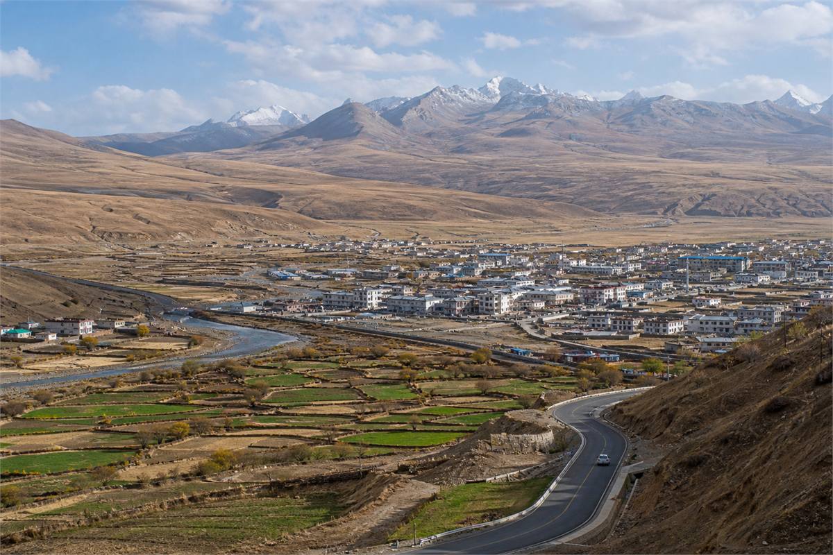 A town, river, cultivated fields, and road spread across a broad Tibetan Plateau valley