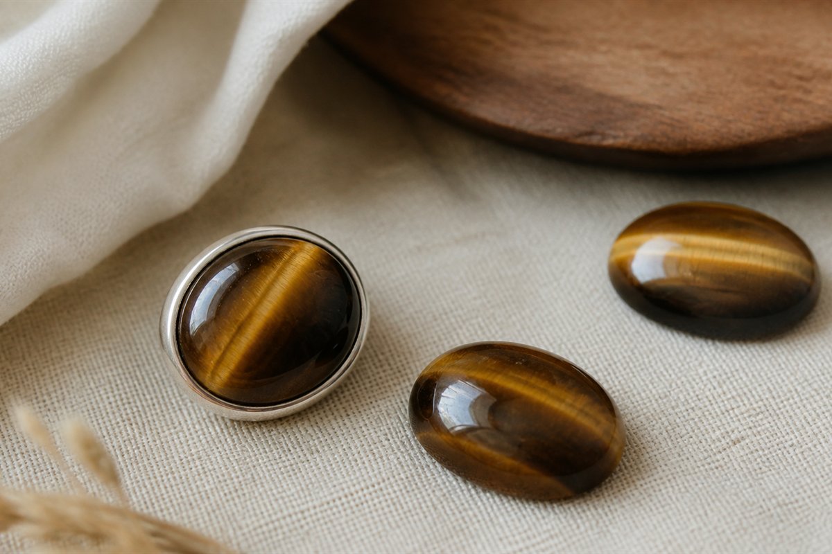 Tiger’s eye cabochon and beads showing a narrow moving band of reflected light across brown-gold surfaces.