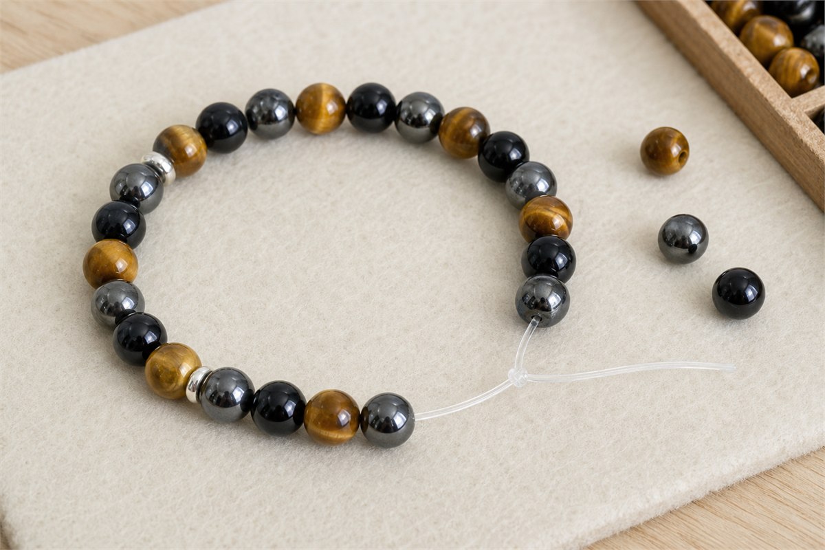 Open tiger’s eye, obsidian and hematite bracelet showing elastic cord, bead holes, knot and spacers