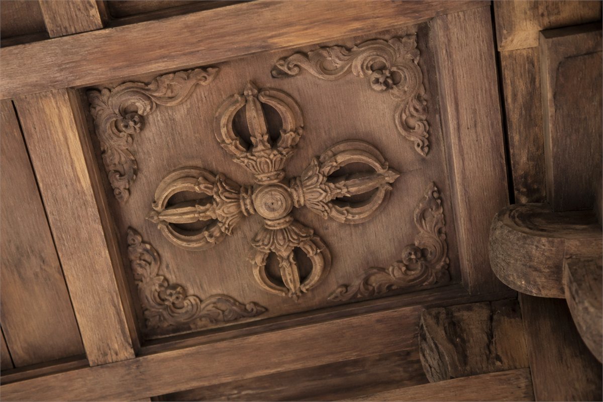 A crossed-vajra motif carved into an aged wooden architectural panel