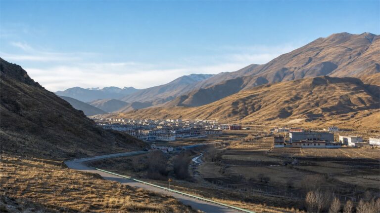 A high plateau valley with a winding road, river, fields, and a small town beneath mountains
