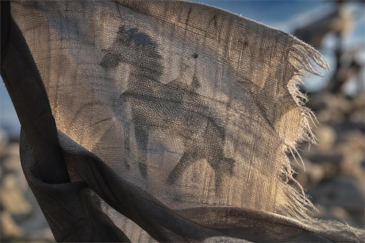 Backlit woven prayer flag cloth with an indistinct horse-shaped print showing through