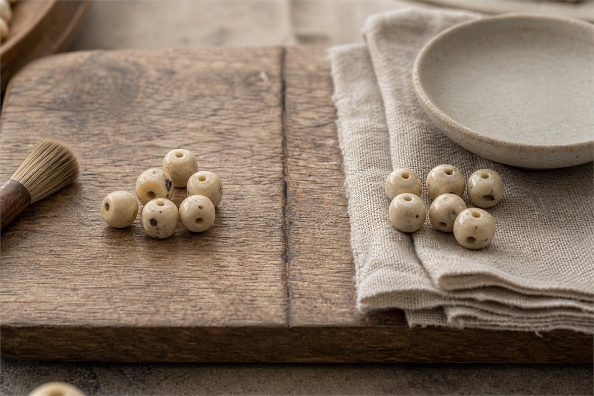 Two neutral groups of Xingyue beads beside a dry brush, linen cloth, and ceramic dish