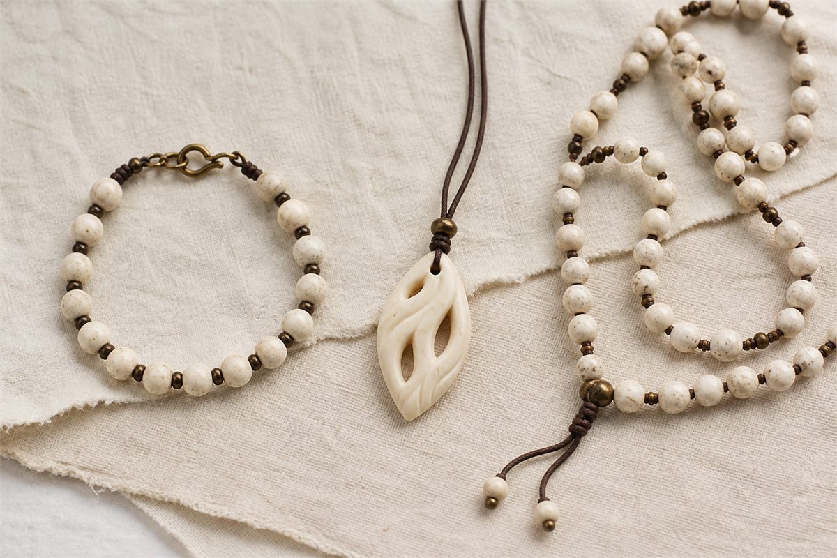Pale bone bracelet, simple carved pendant, and long decorative bead strand on linen