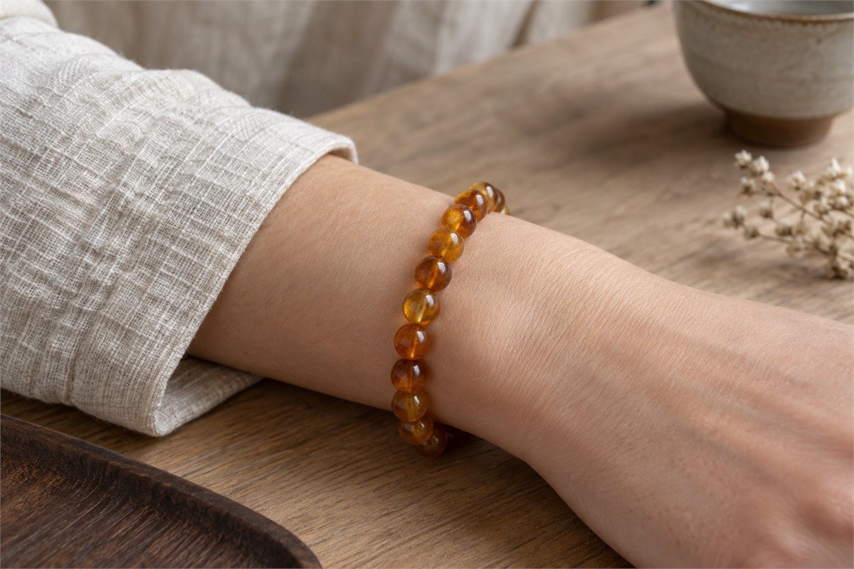 A simple amber bead bracelet worn loosely on a relaxed wrist beside a linen sleeve.