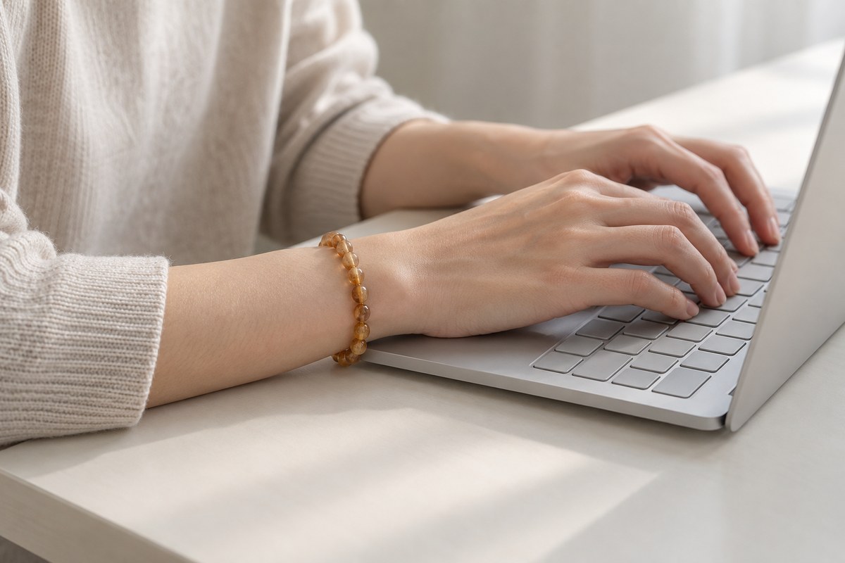 A small amber bracelet sits on an adult wrist beside a laptop.
