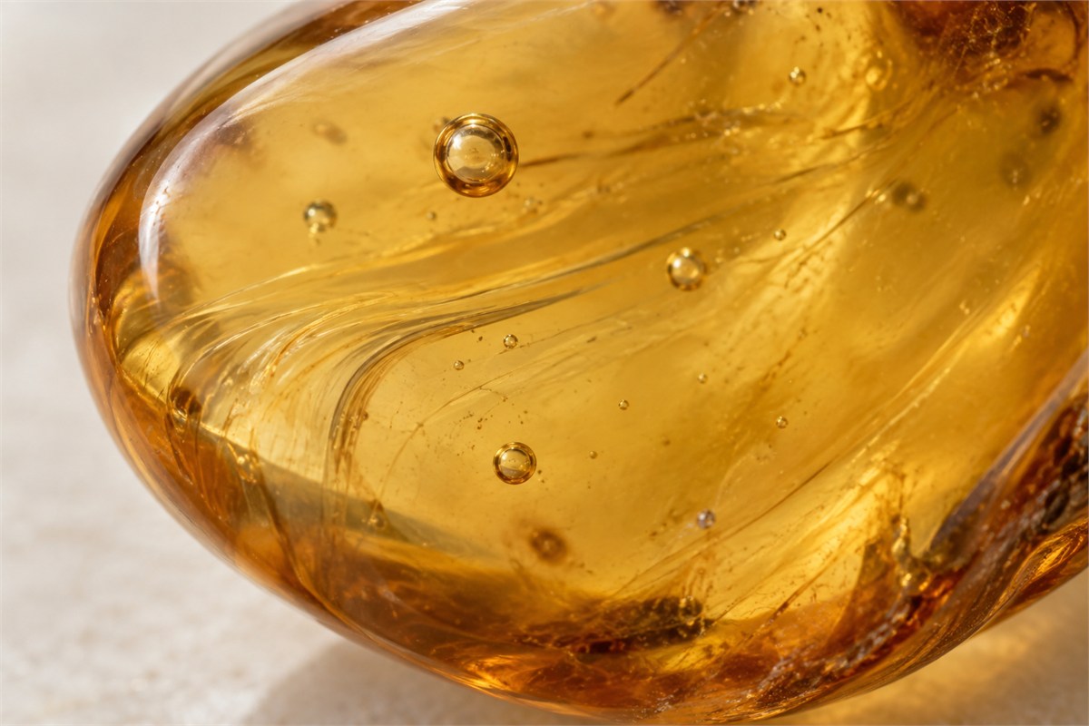 Fine curved flow lines and scattered small bubbles in a honey-colored amber close-up.