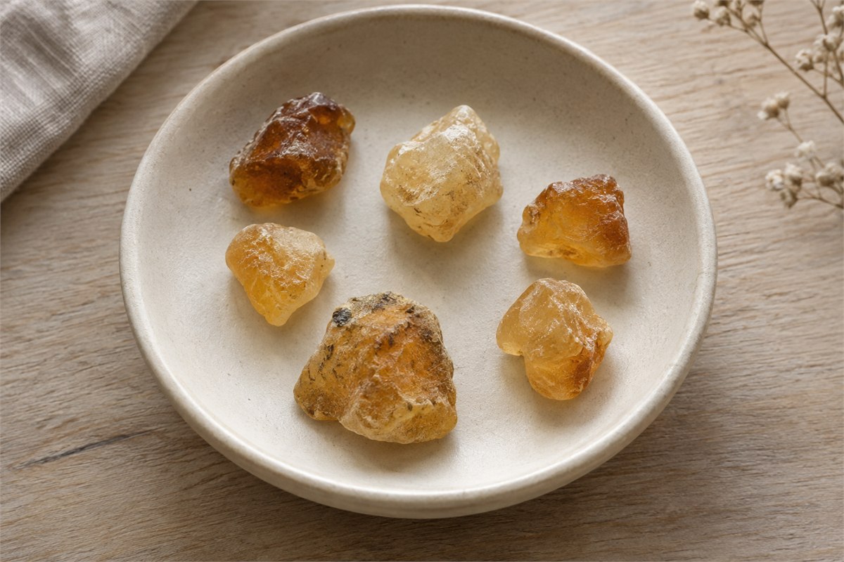 Six small irregular golden resin fragments rest in a shallow ceramic dish.