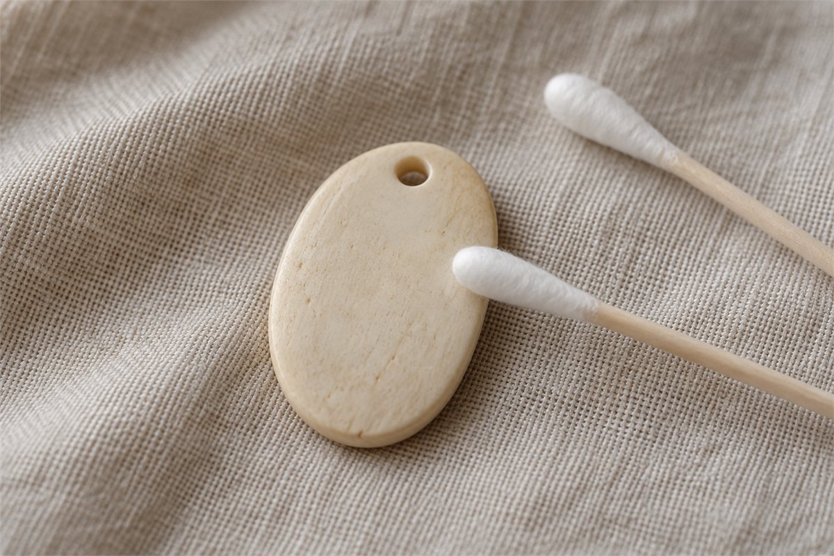 Two cotton swabs beside a smooth pale pendant on dry cloth.