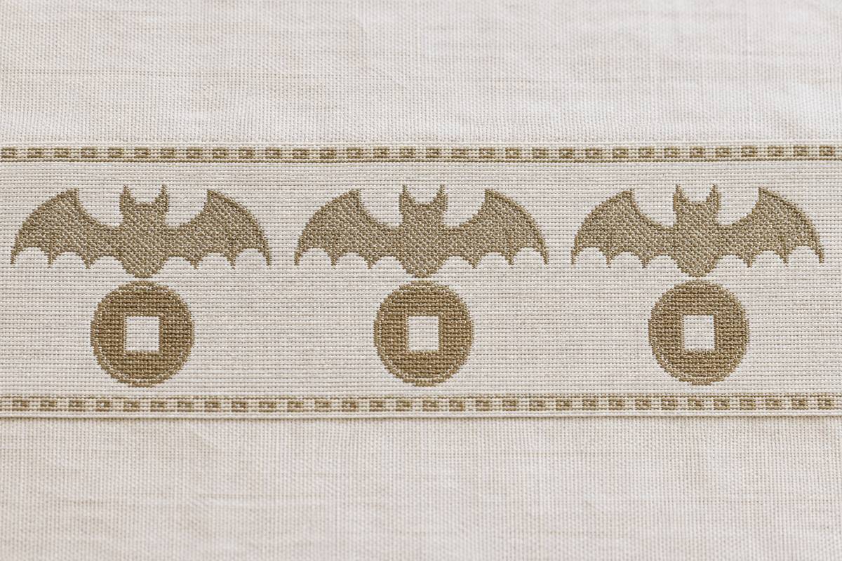 Woven fabric border repeating three bat-and-coin motifs in muted colors.