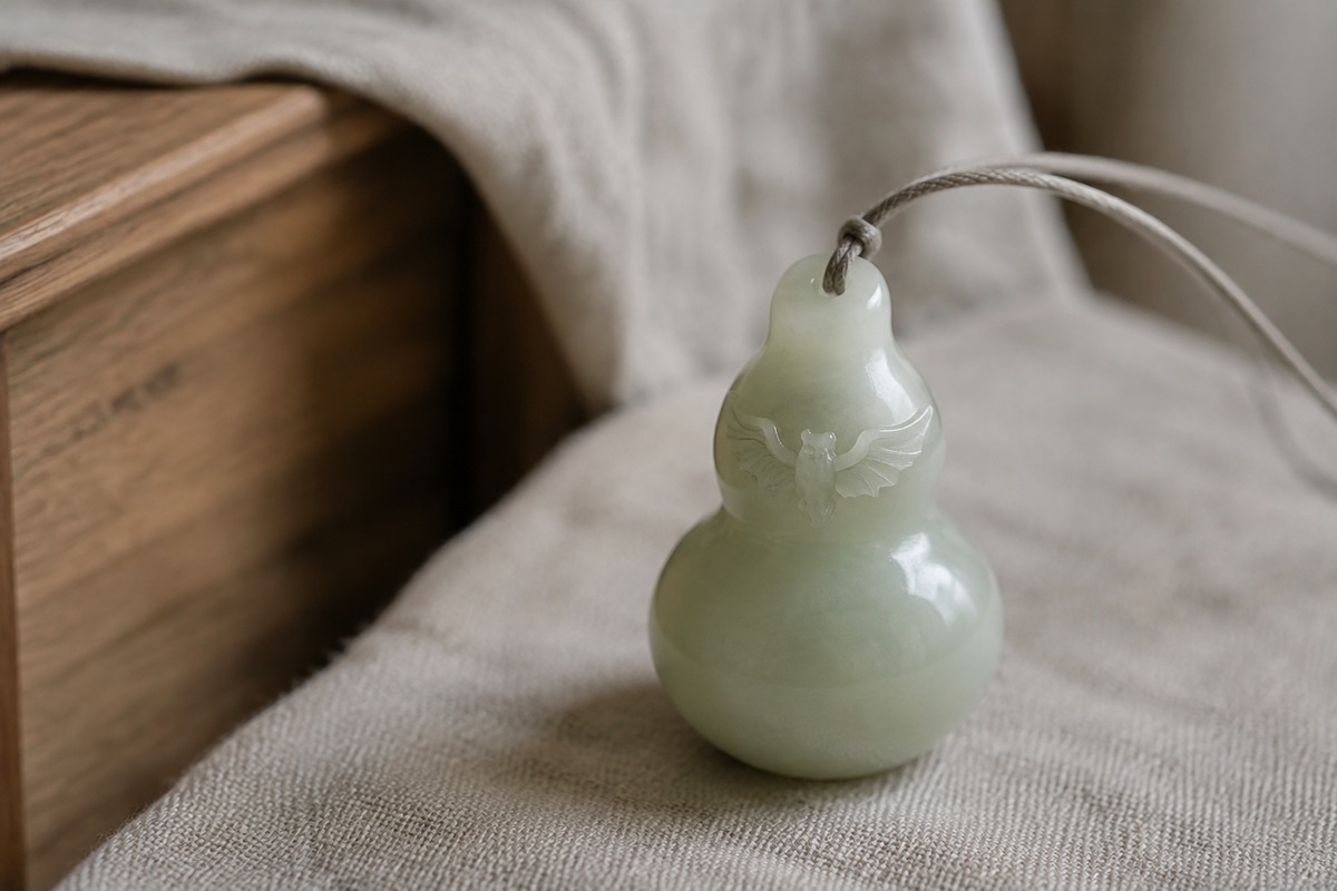 Small pale green gourd pendant with a single bat carved across its shoulder.