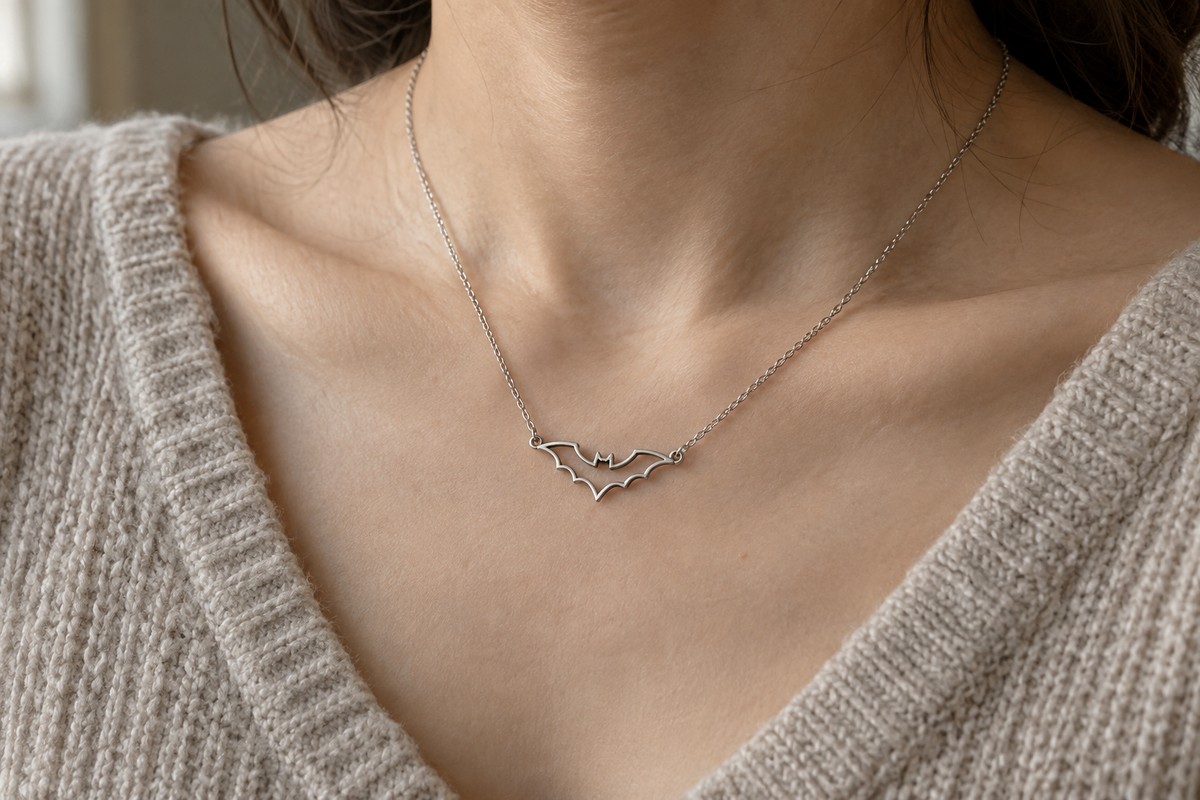 Small silver-colored bat outline necklace worn with an oatmeal knit top