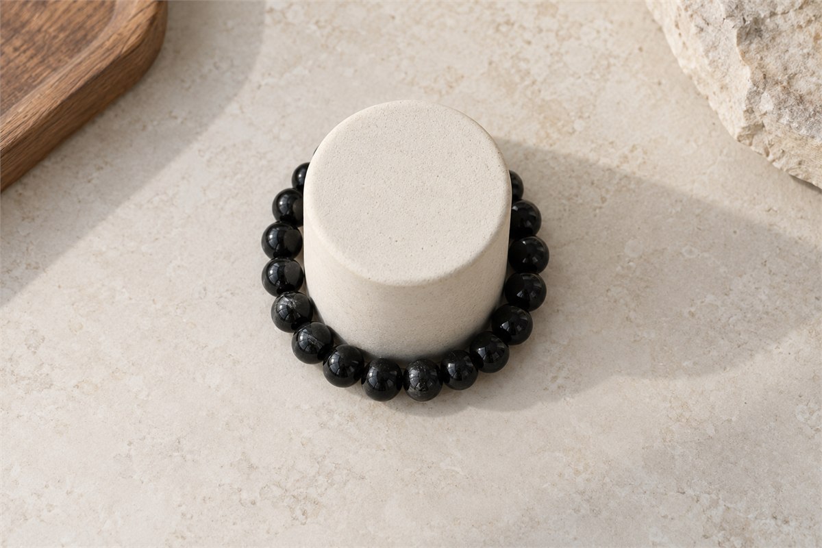 A black tourmaline bracelet resting around a plain cylindrical bracelet stand.