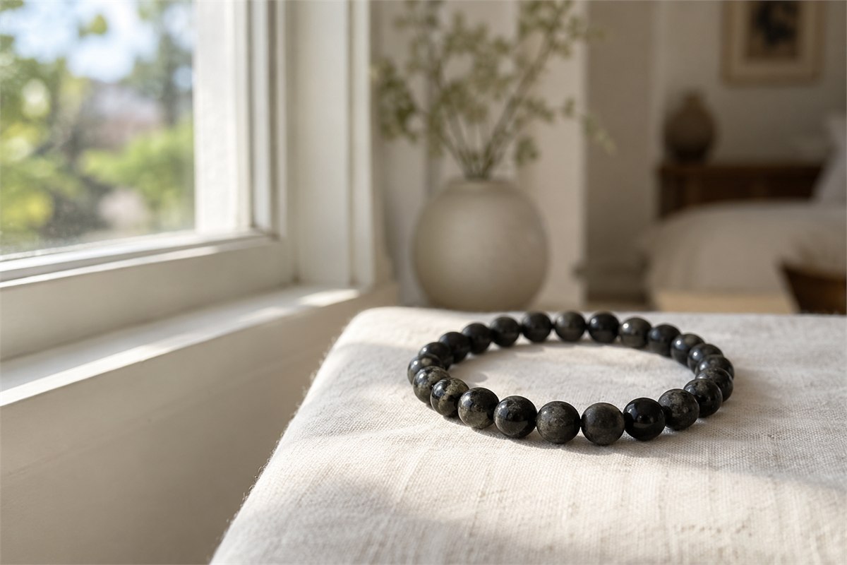 A slim black tourmaline bracelet on ivory linen beside a softly lit window.