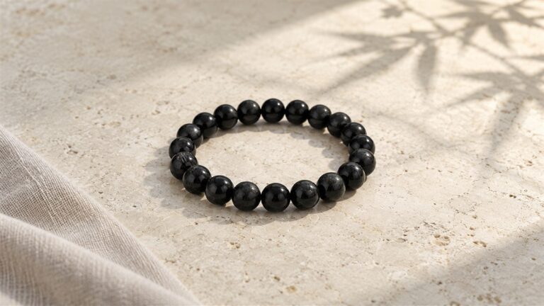 A black tourmaline bracelet on pale limestone with linen and a quiet bamboo shadow.