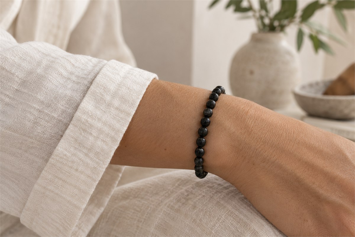 A slender black tourmaline bracelet beside a soft ivory sleeve.