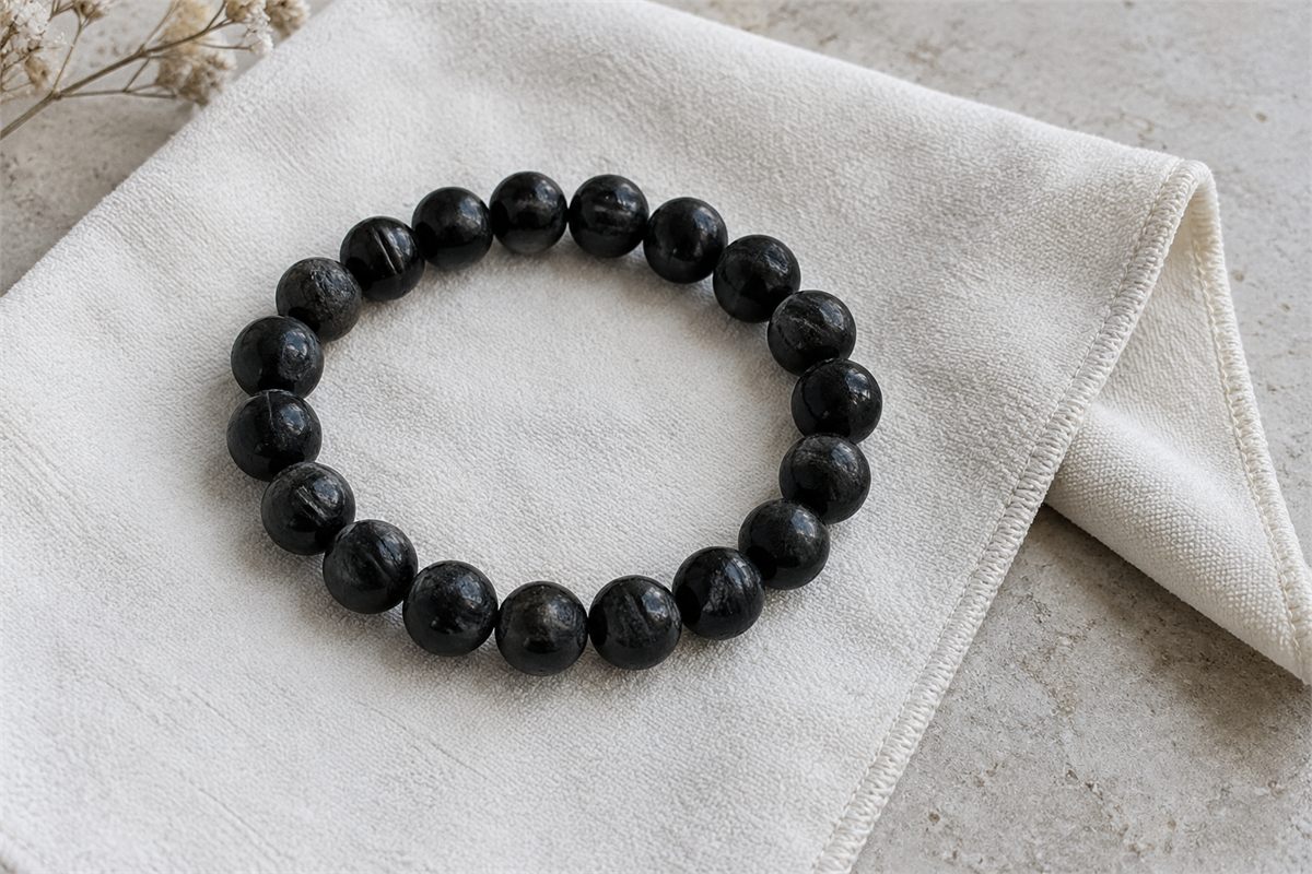A black tourmaline bracelet resting on a clean pale microfiber cloth.