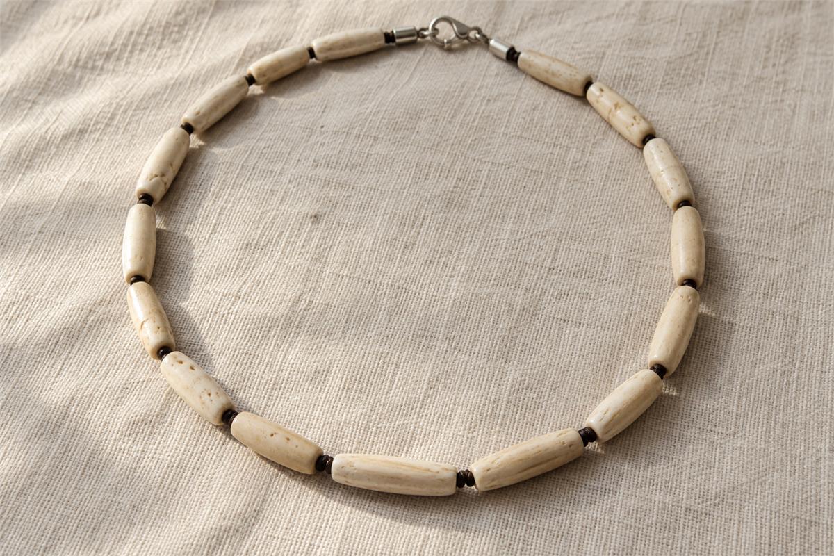 Pale bead necklace with a cord and silver-colored clasp on linen.