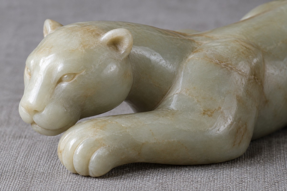 Close view of a rounded jade chi head, small ears, broad muzzle, and bent front paw.