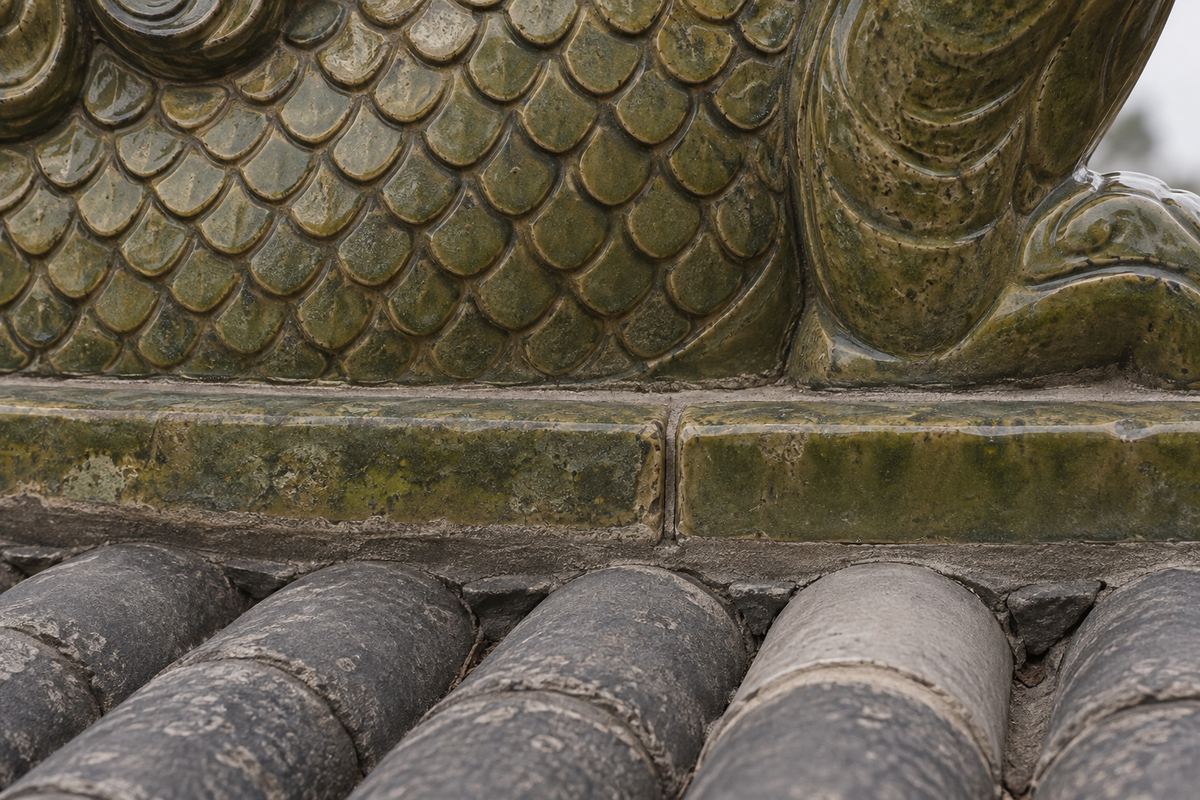 Close view of a glazed ceramic ridge ornament base and fitted seam above renewed roof tiles
