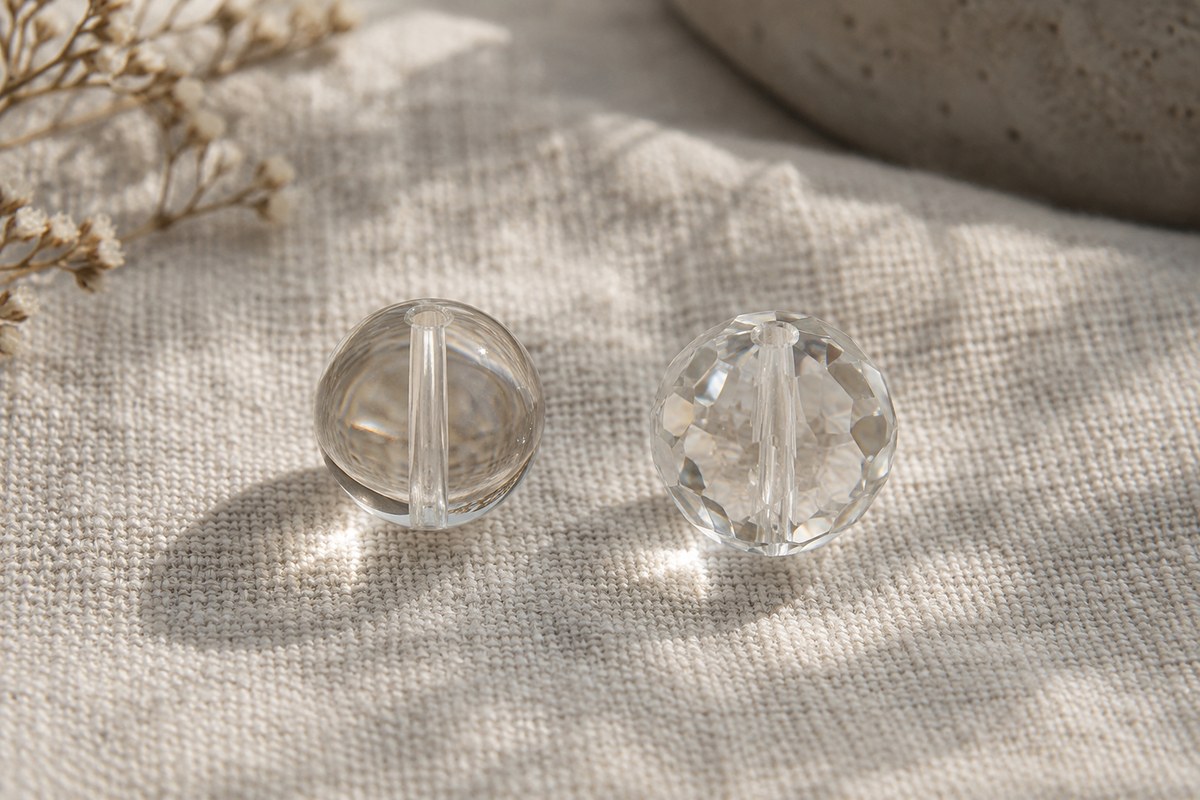 A round clear bead and a faceted clear bead resting separately on woven linen.
