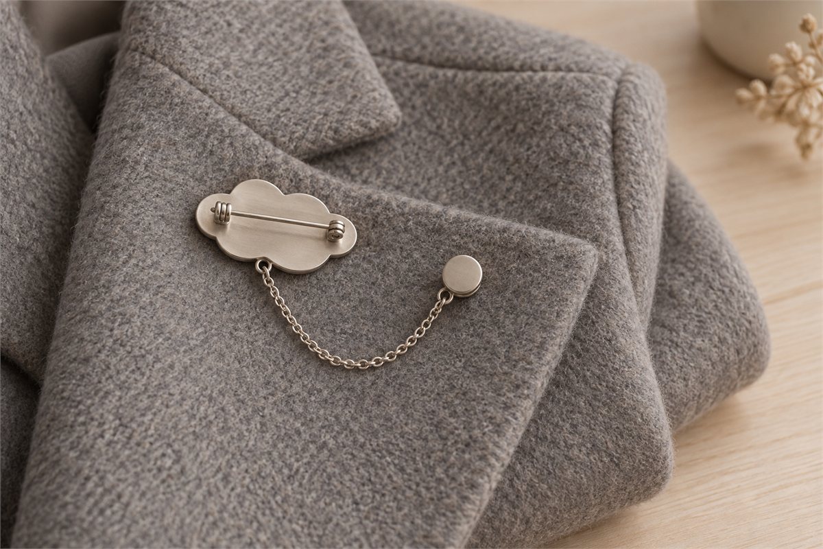 The reverse of a cloud-shaped brooch shows a closed pin and a softly draped lapel chain.