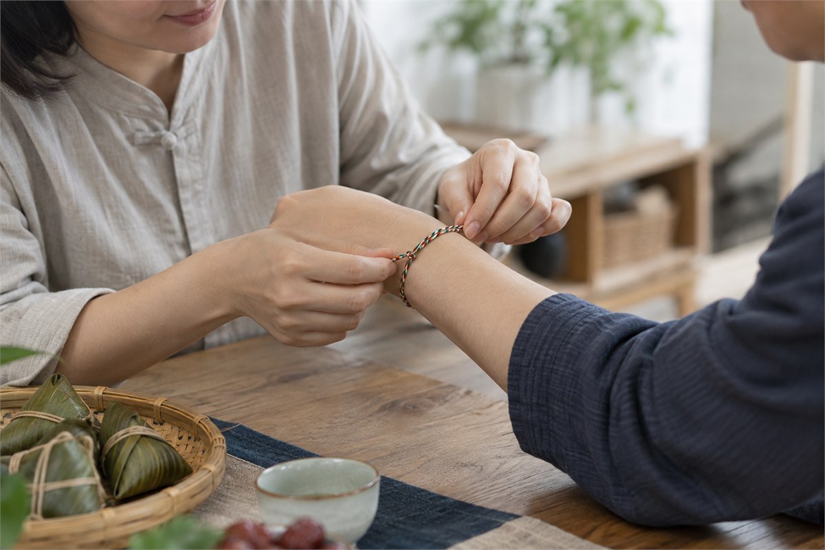 An adult gently tying a five-color cord around another adult’s wrist