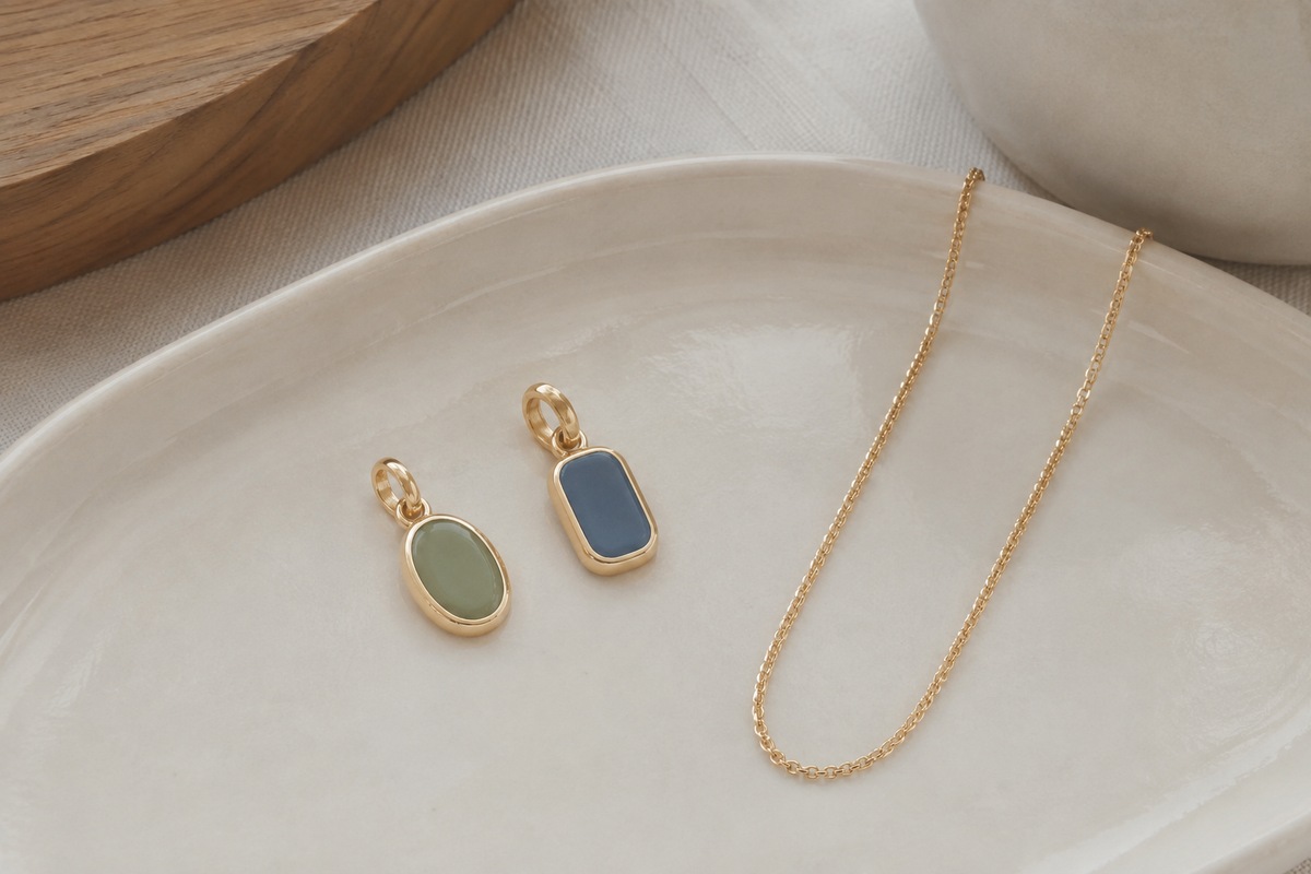 Two small gold-colored pendants with muted green and blue enamel lie side by side.