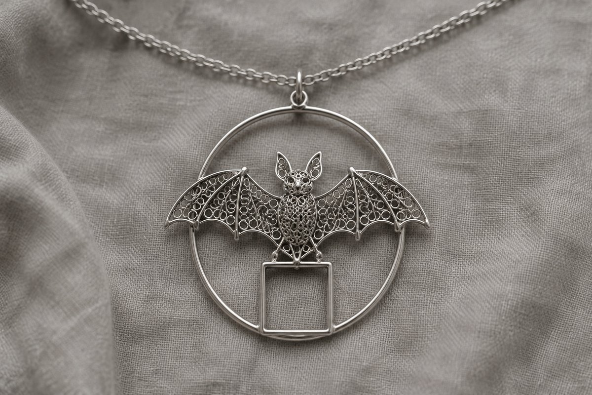 Fine wirework bat-and-coin pendant on a chain against gray linen.