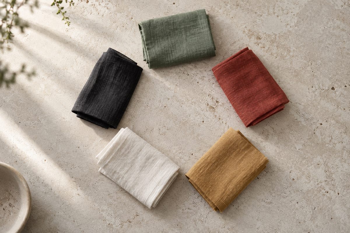 Five small folded textile strips in green, red, yellow, white and black form a loose circle on pale stone.