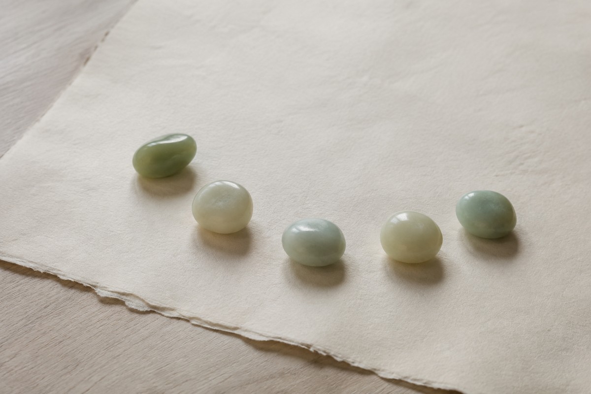 Five rounded green and cream stones arranged on textured ivory paper.