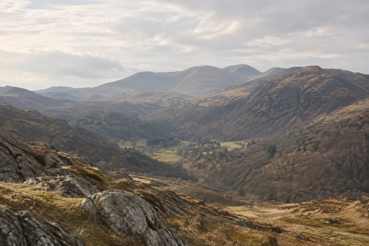 Rounded mountain ridges overlooking a calm valley under a pale sky.